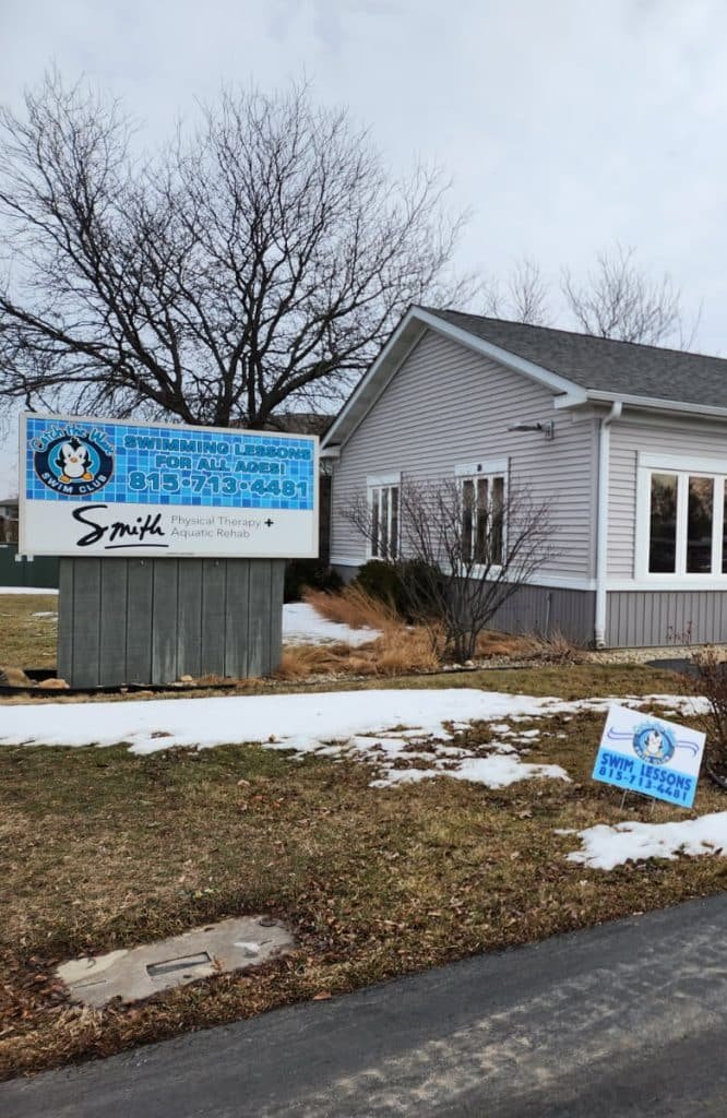 A light gray building with white trim and a large sign advertising "SWIMMING LESSONS FOR ALL AGES!"