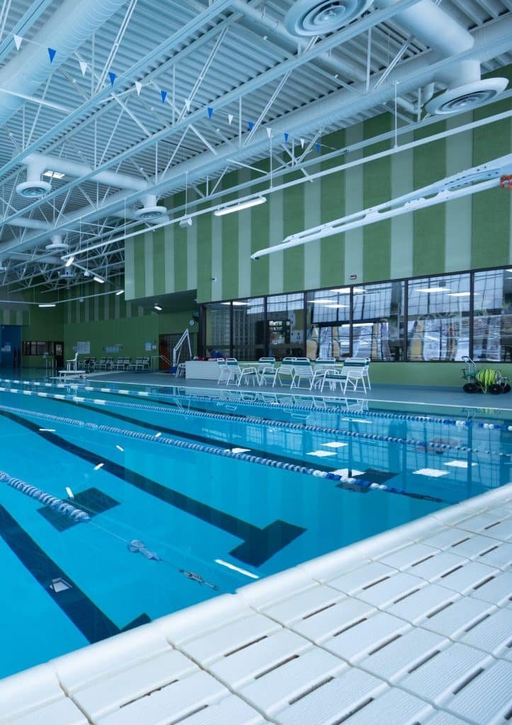 An indoor swimming pool with blue lanes, a white tiled ceiling, and green striped walls.