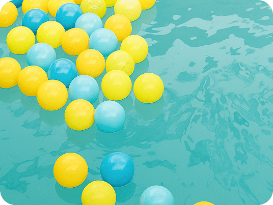 Numerous yellow and blue plastic balls float on a turquoise water surface with ripples.