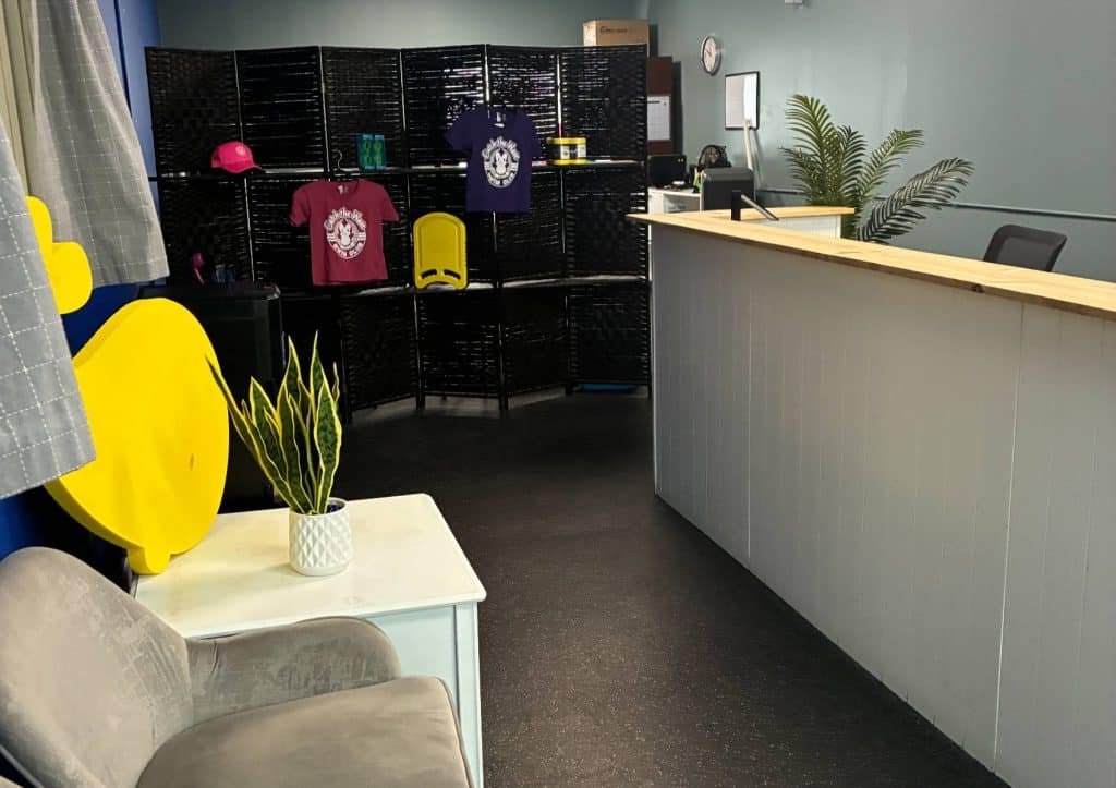 A light gray reception desk with a wooden top stands in a room with a black divider displaying t-shirts.